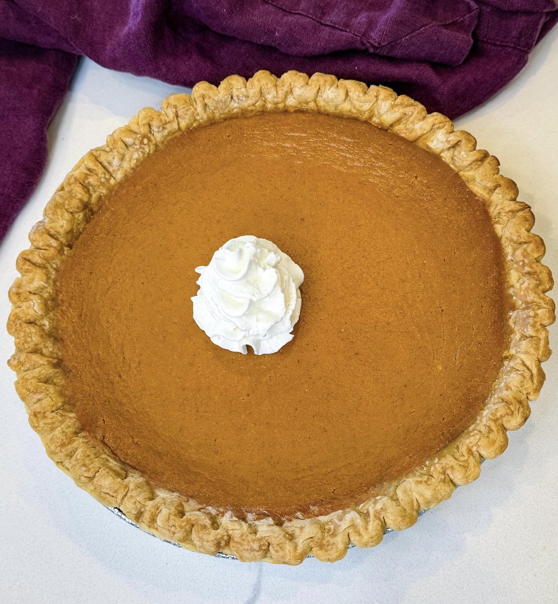 Whole pumpkin pie baked in a golden frozen crust and topped with whipped cream in the center.