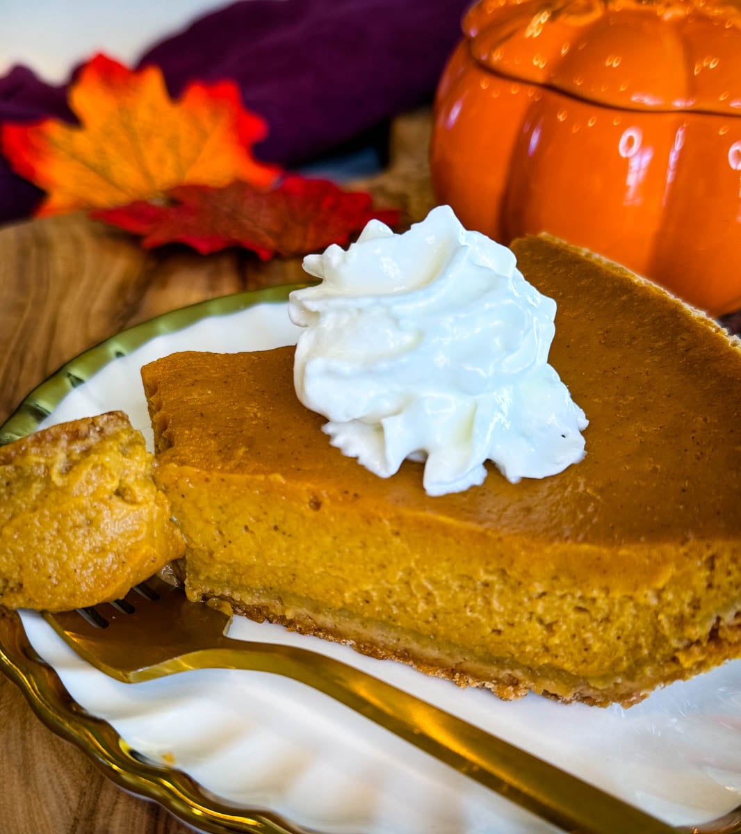 Close-up of creamy pumpkin pie with graham cracker crust and whipped cream, showing the smooth spiced pumpkin filling.