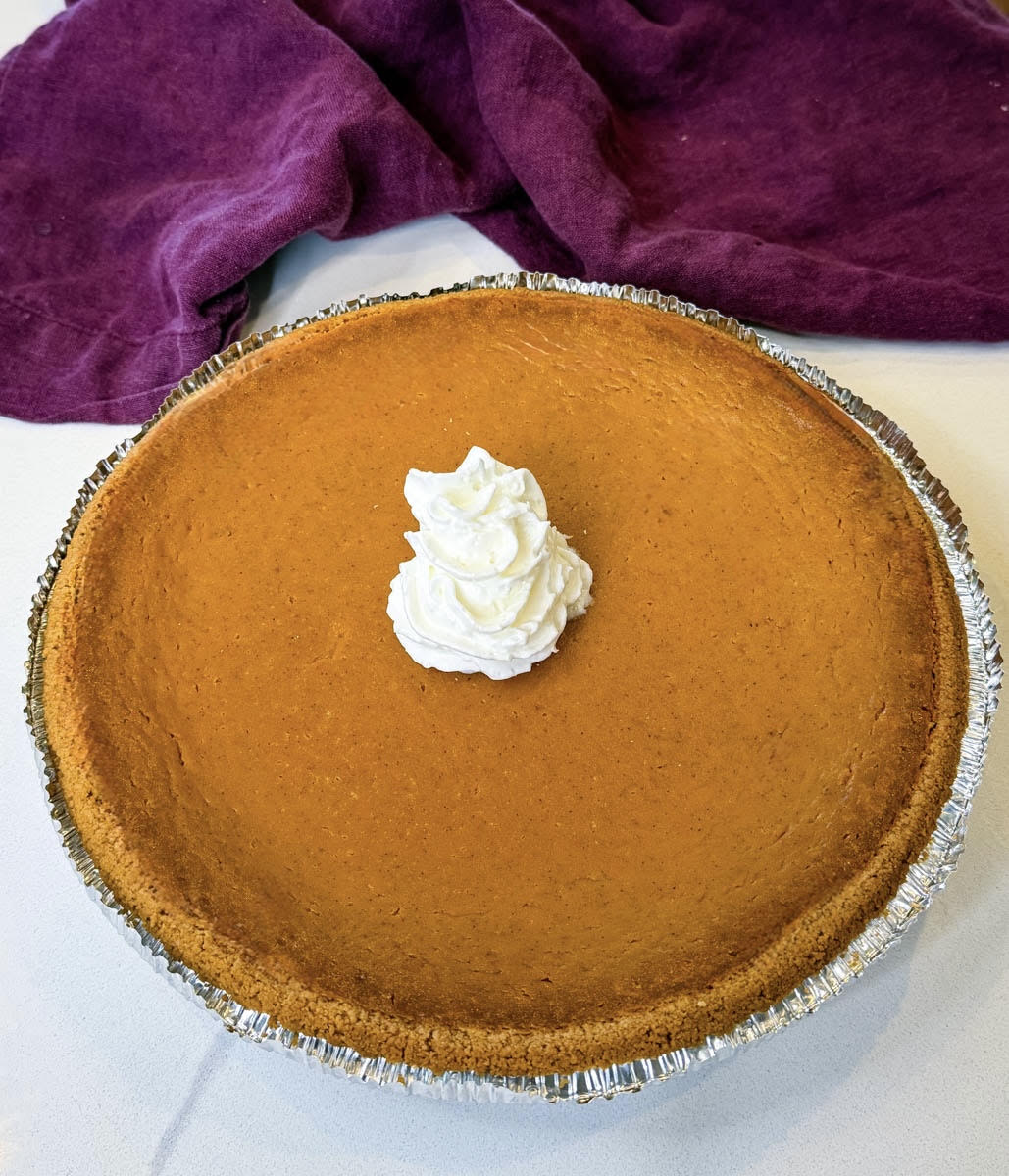 Whole pumpkin pie with graham cracker crust topped with whipped cream in the center.