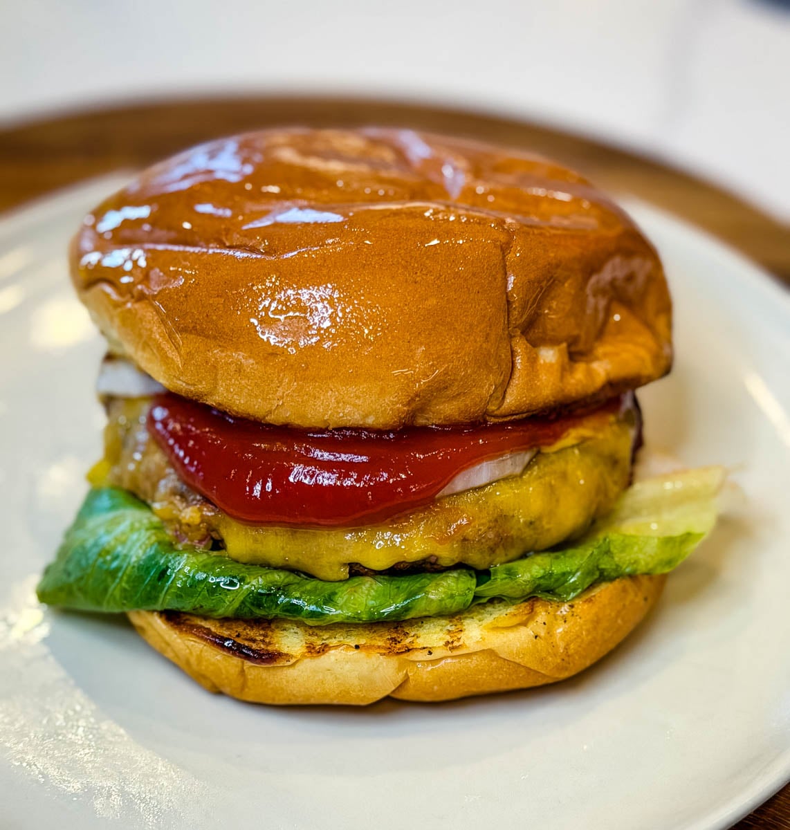 Homemade smashburger on a toasted bun topped with melted cheese, lettuce, onion, pickles, and ketchup.