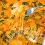 Close-up of cheesy chicken broccoli rice casserole with a fork lifting a bite of chicken, broccoli, and rice with melted cheddar cheese stretching from the baking dish.