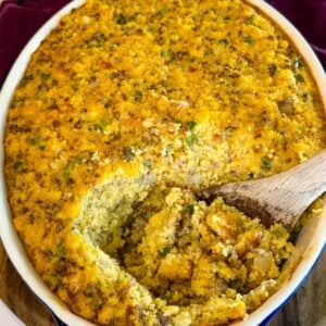 Baked cornbread dressing with sausage and vegetables in a casserole dish with a serving spoon revealing the moist interior.