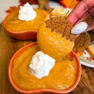 Ginger cookie dipped into creamy pumpkin pie dip served in an orange pumpkin-shaped bowl with whipped topping.