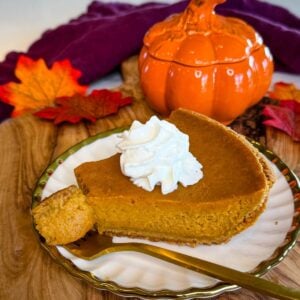 Slice of pumpkin pie with graham cracker crust topped with whipped cream and served with a gold fork.