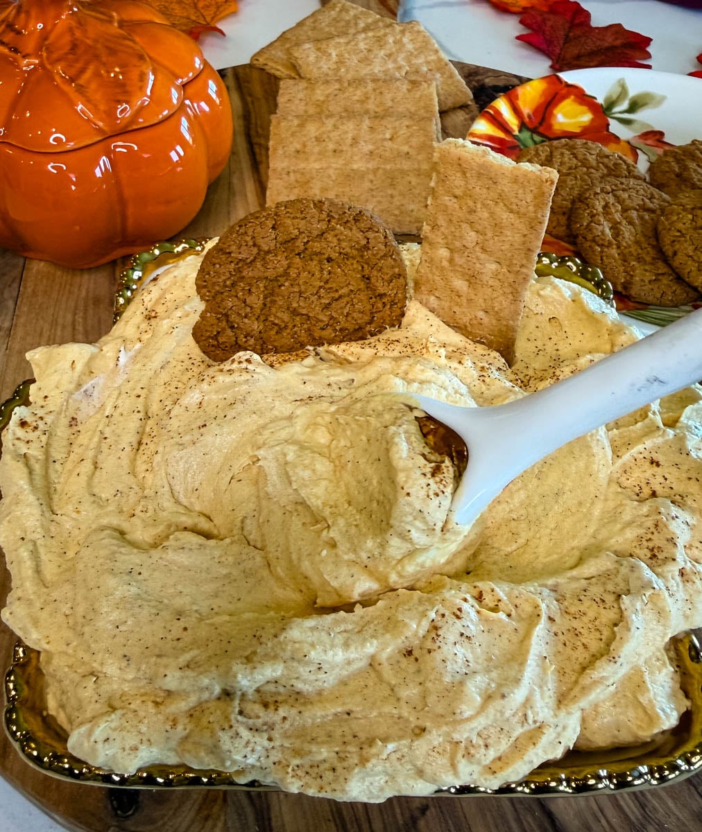 Creamy pumpkin cheesecake dip topped with pumpkin spice and served with graham crackers and ginger cookies on a fall-themed platter.