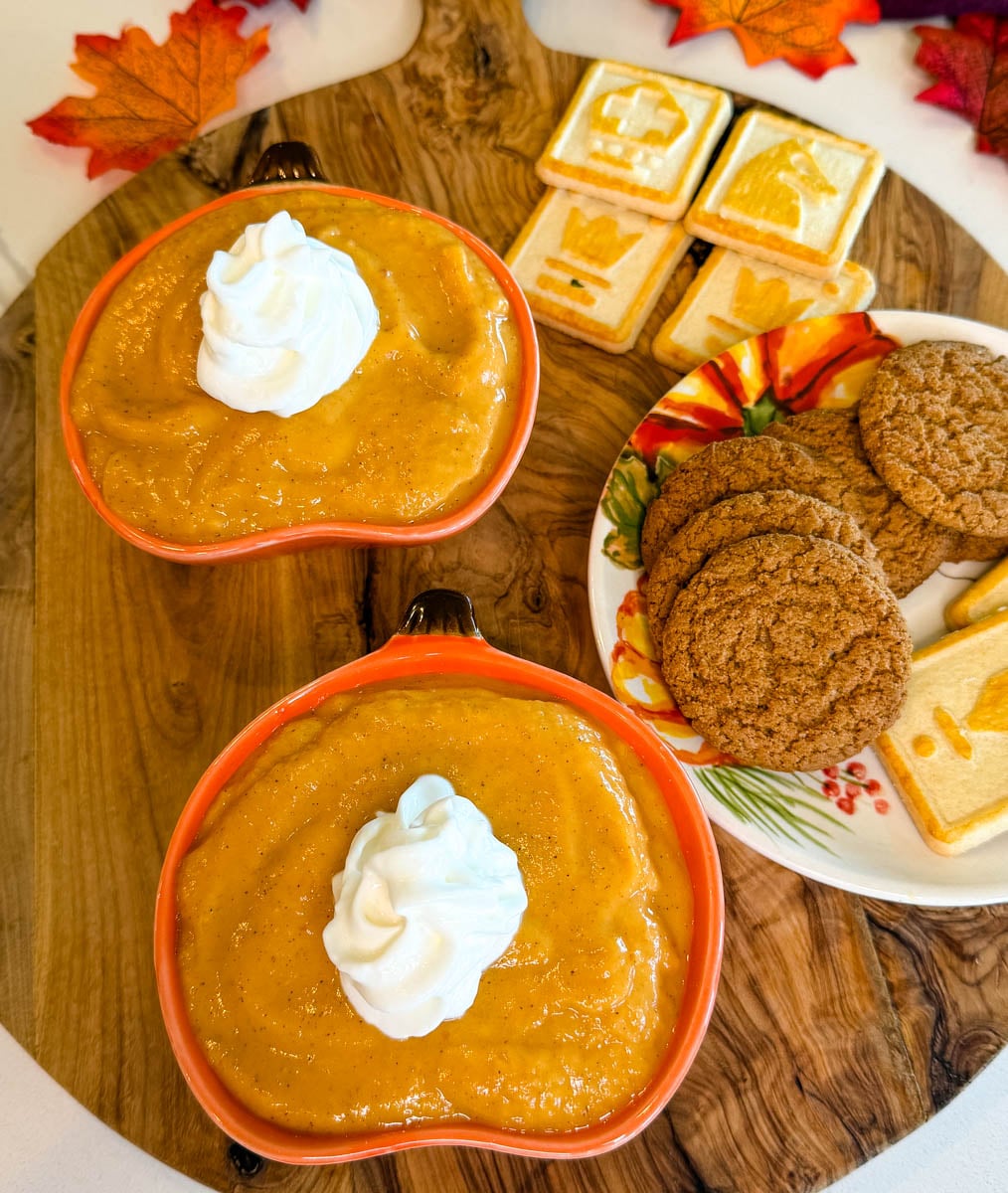 Two bowls of creamy pumpkin pie dip topped with whipped cream and served alongside ginger cookies and fall-themed cookies.