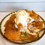 Southern peach cobbler served warm on a plate with tender peaches, flaky golden pie crust, vanilla ice cream, and peach syrup drizzled over the top.