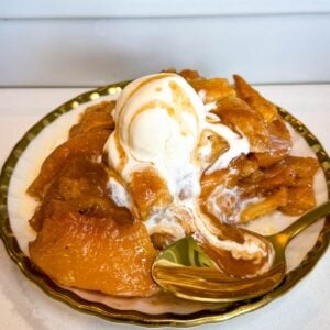 Southern peach cobbler served warm on a plate with tender peaches, flaky golden pie crust, vanilla ice cream, and peach syrup drizzled over the top.