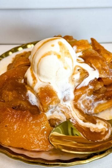 Southern peach cobbler served warm on a plate with tender peaches, flaky golden pie crust, vanilla ice cream, and peach syrup drizzled over the top.