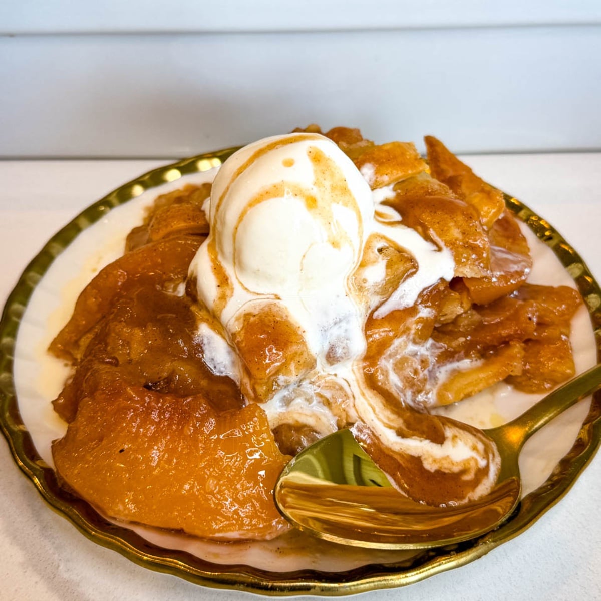 Southern peach cobbler served warm on a plate with tender peaches, flaky golden pie crust, vanilla ice cream, and peach syrup drizzled over the top.