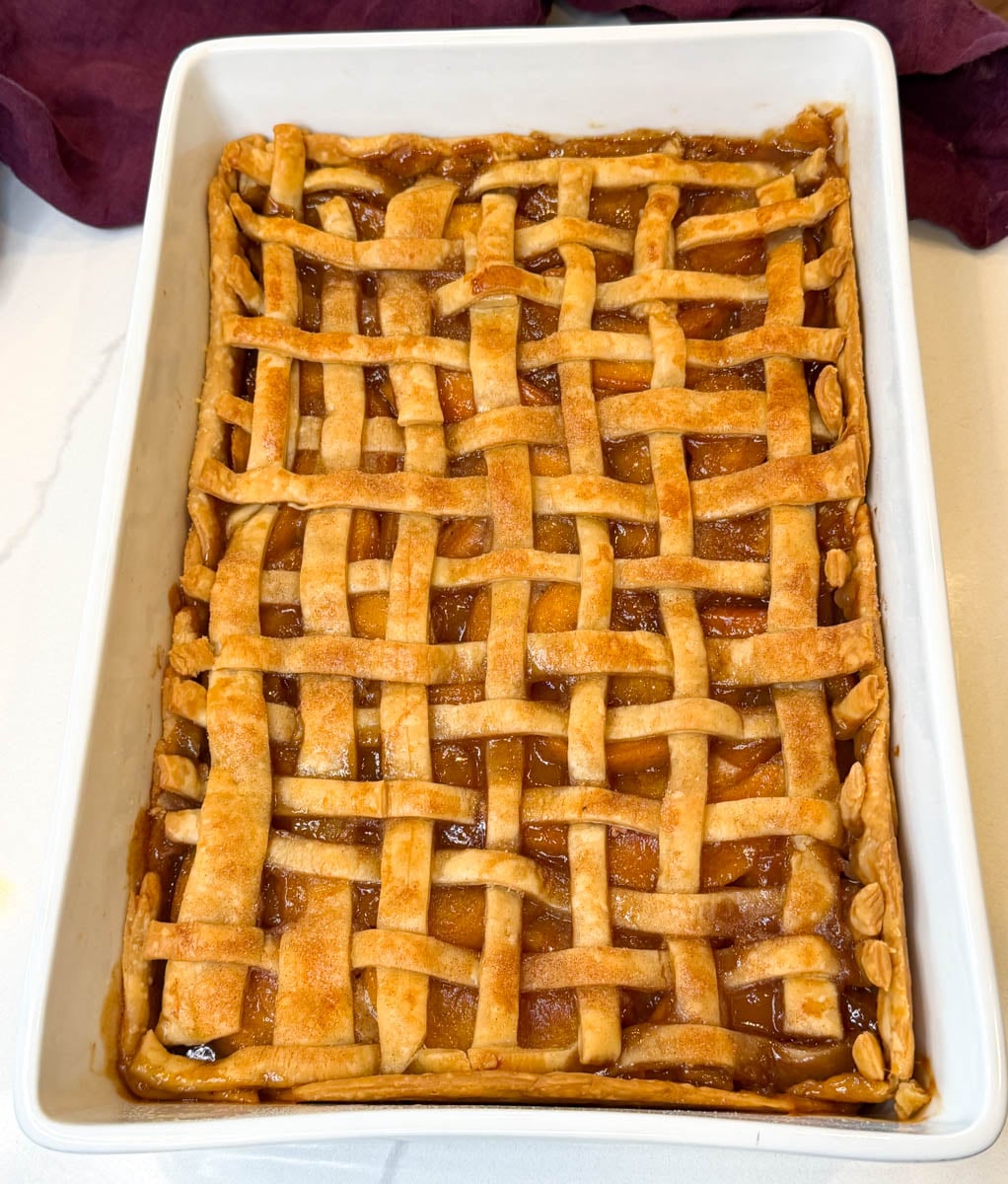 Baked Southern peach cobbler in a rectangular dish with a golden brown lattice pie crust and peach filling bubbling between the crust strips.