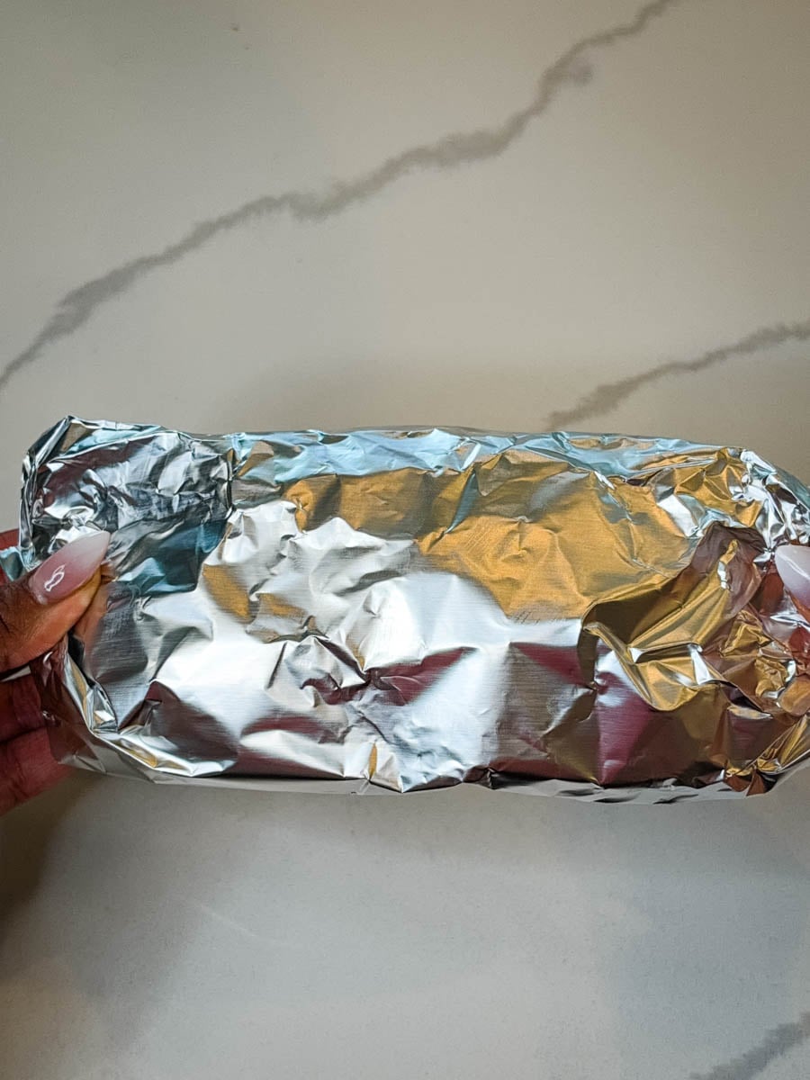 Foil-wrapped croissant breakfast sandwich held in both hands, ready for storing, freezing, or reheating.