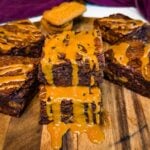 Two thick Biscoff brownie squares stacked on a wooden board, showing fudgy chocolate centers and cookie pieces with melted cookie butter dripping over the brownies.