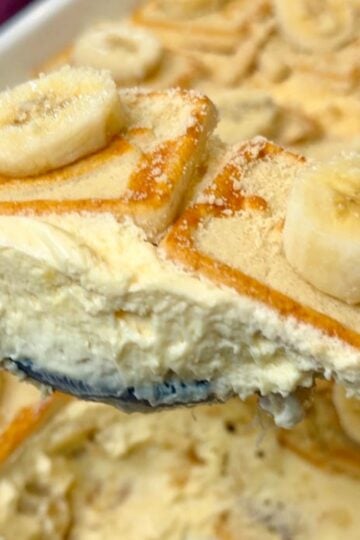 Close-up of a spoonful of creamy Chessman banana pudding with layers of banana, pudding, and cookies, with the finished dessert in the background.