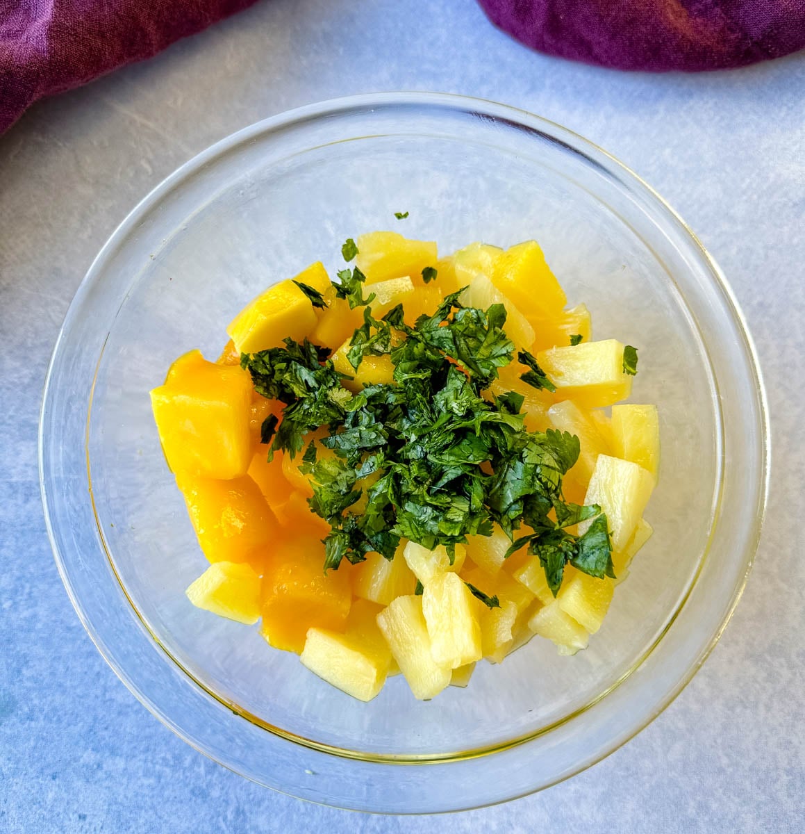 Pineapple and mango chunks topped with freshly chopped cilantro in a glass bowl for homemade pineapple mango salsa.