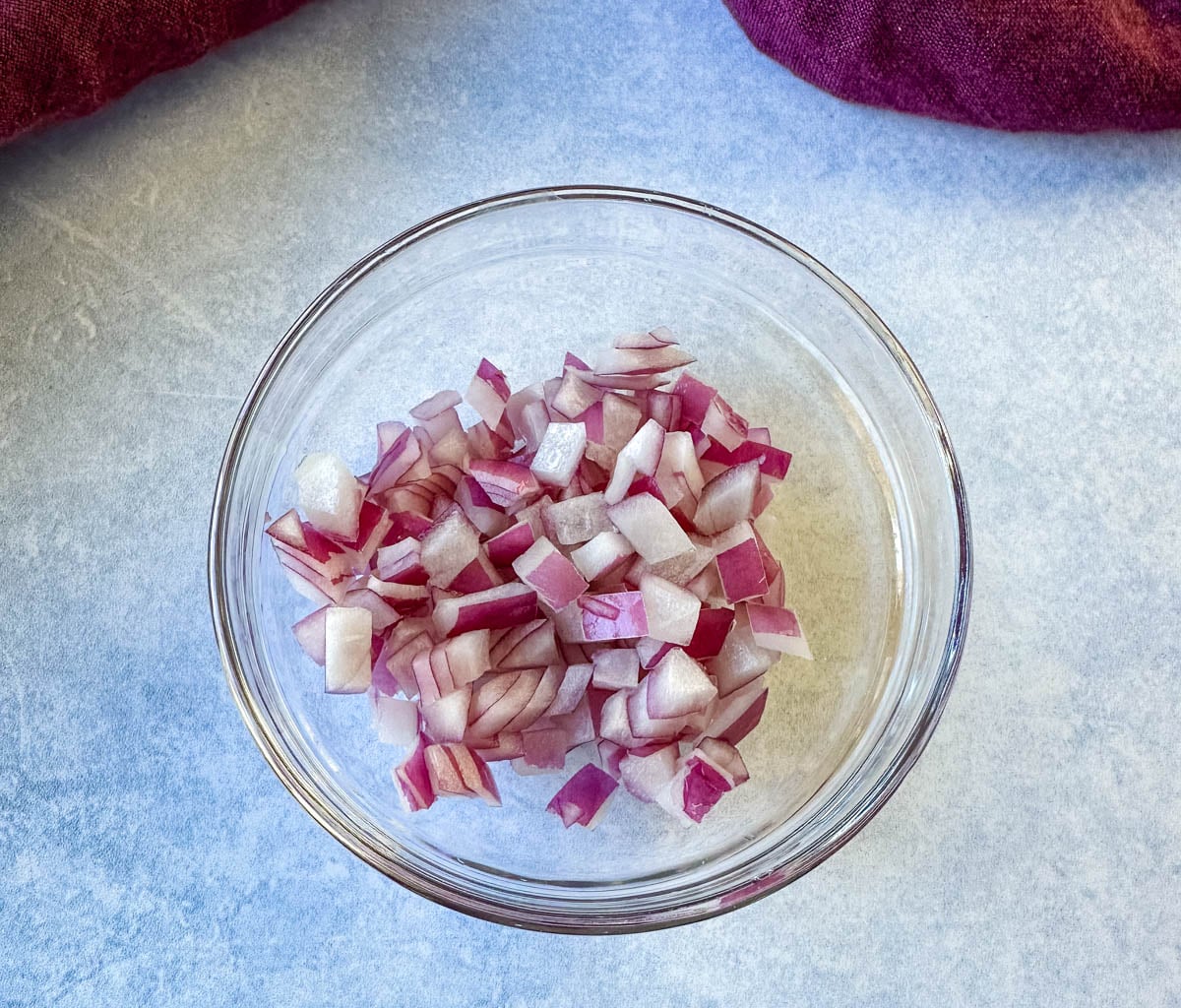 Chopped red onion in a small glass bowl for pineapple mango salsa.