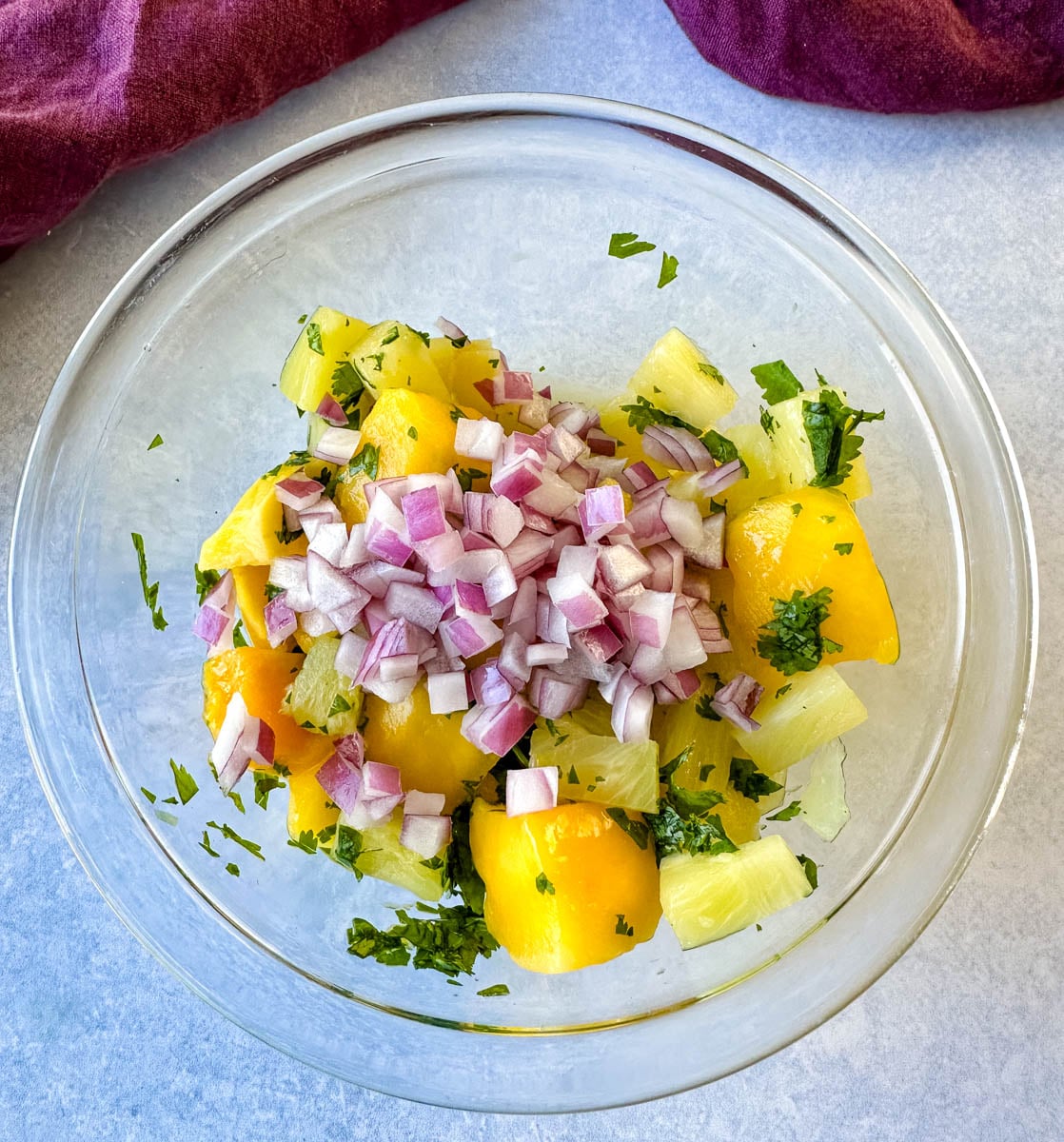 Fresh pineapple, mango, cilantro, and chopped red onion combined in a glass bowl before mixing the pineapple mango salsa.
