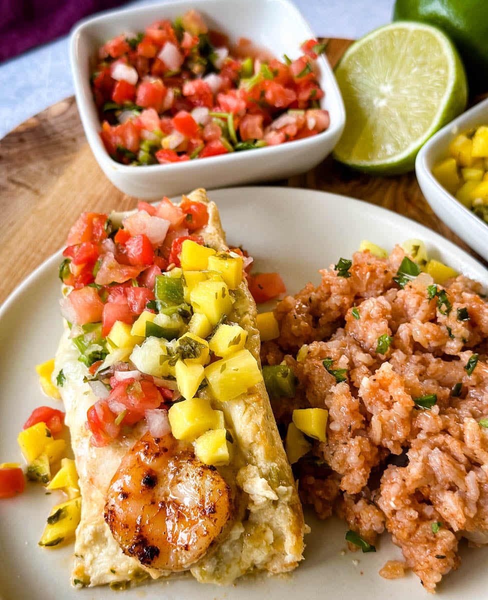 Creamy shrimp enchilada topped with seasoned shrimp, pico de gallo, and fresh mango salsa, served with Mexican-style rice and fresh lime.