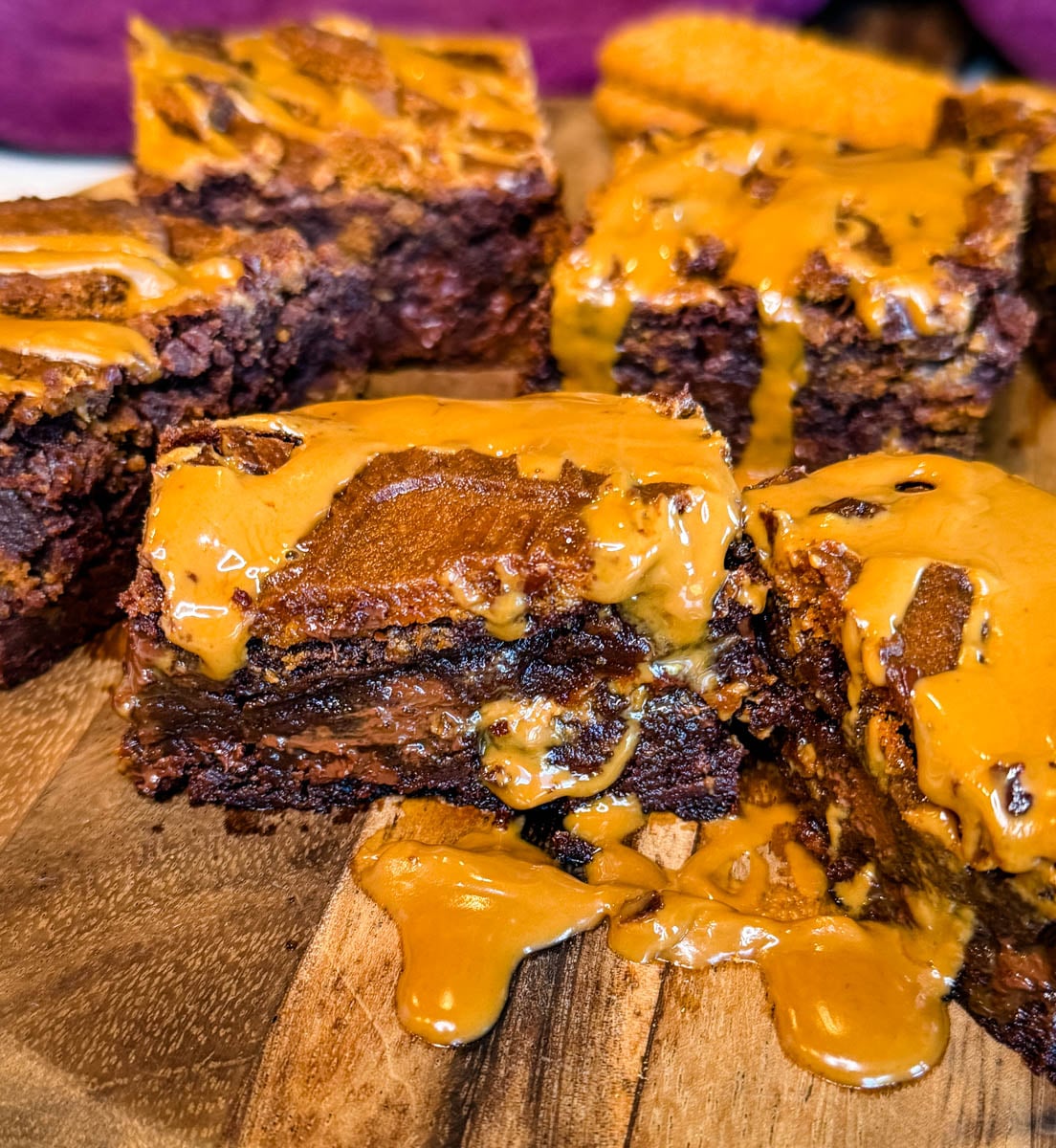 Close-up of thick, fudgy Biscoff brownies stacked on a wooden board with visible cookie butter layers, Biscoff cookie pieces, and melted cookie butter drizzled over the top.