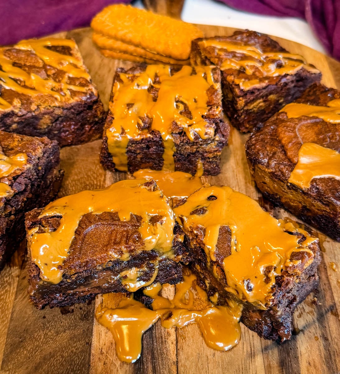 Overhead view of Biscoff brownie squares arranged on a round wooden serving board with Biscoff cookies and melted cookie butter drizzled over the tops.