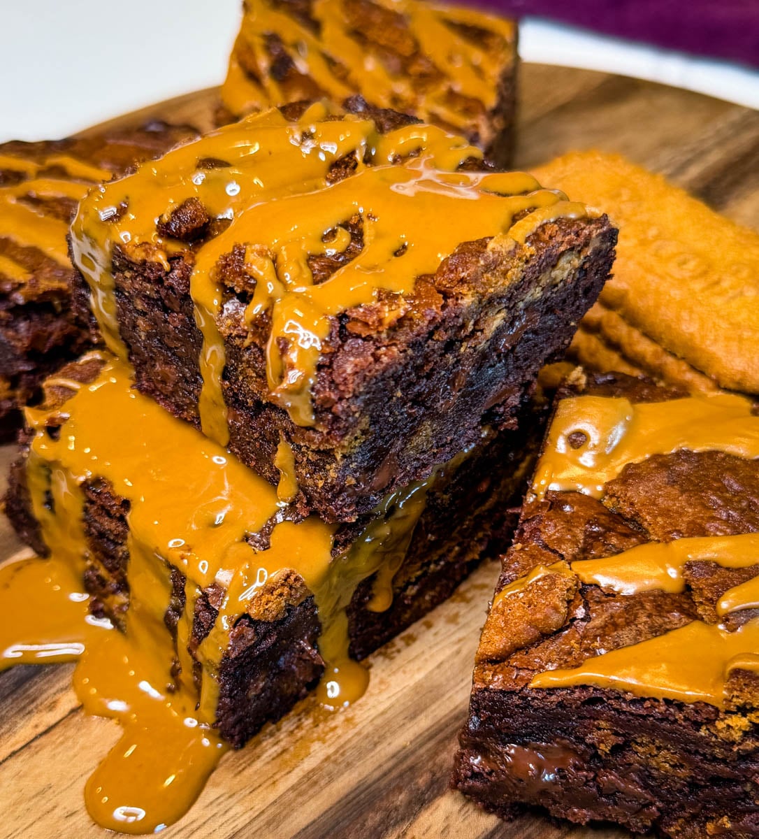 Close-up of stacked Biscoff brownies with gooey chocolate centers, crushed Biscoff cookies, and melted cookie butter dripping down the sides.