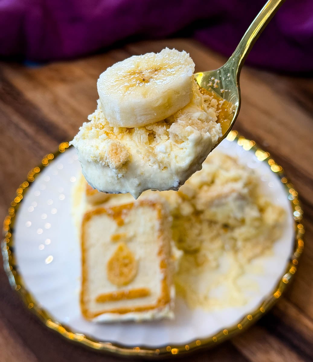 Close-up of a spoonful of creamy Chessman banana pudding topped with a fresh banana slice and crushed cookies.